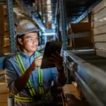 Warehouse manager monitoring inventory using barcode scanner and inventory management software in a modern warehouse.